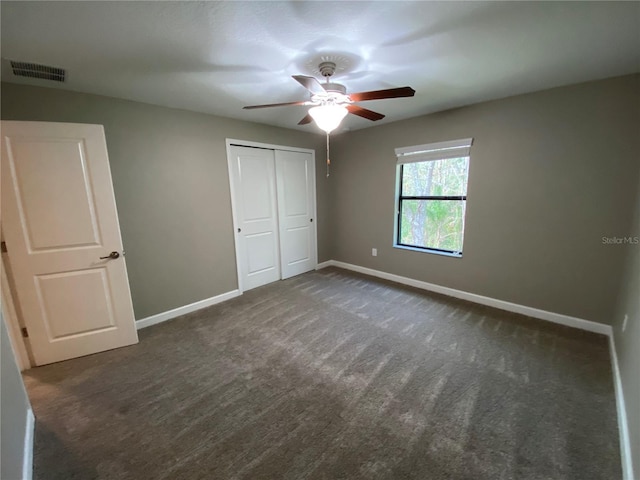 unfurnished bedroom with ceiling fan, a closet, and dark colored carpet