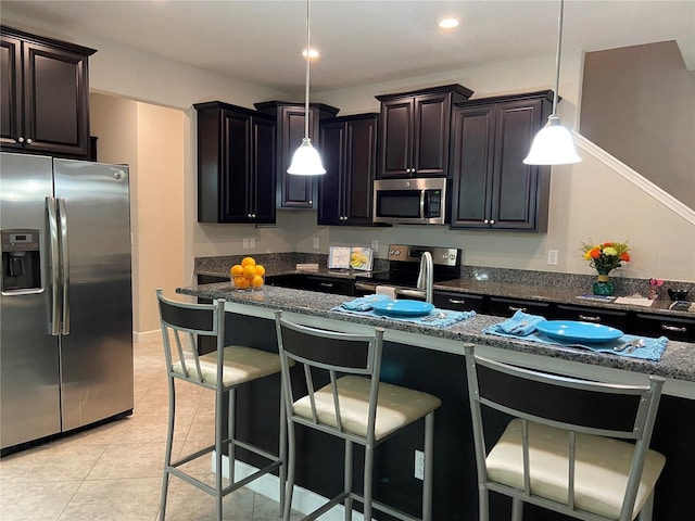 kitchen with light tile patterned floors, dark stone countertops, appliances with stainless steel finishes, a kitchen breakfast bar, and pendant lighting