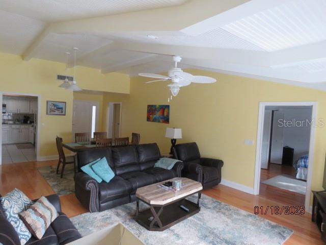 living room featuring light wood-type flooring, ceiling fan, and vaulted ceiling with beams