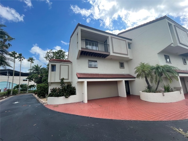 view of front of house featuring a balcony, stucco siding, a garage, a tile roof, and decorative driveway