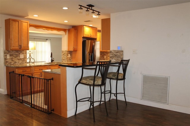 kitchen with sink, light stone counters, stainless steel refrigerator with ice dispenser, kitchen peninsula, and a kitchen bar