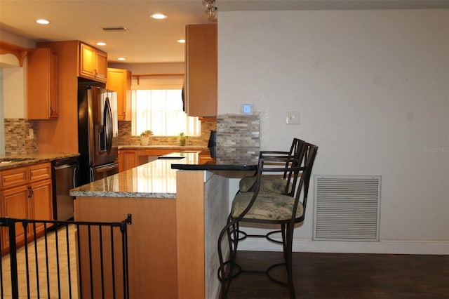 kitchen with a kitchen bar, appliances with stainless steel finishes, backsplash, dark hardwood / wood-style flooring, and light stone countertops