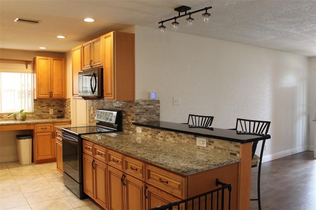 kitchen with a kitchen breakfast bar, electric range oven, dark stone countertops, and decorative backsplash