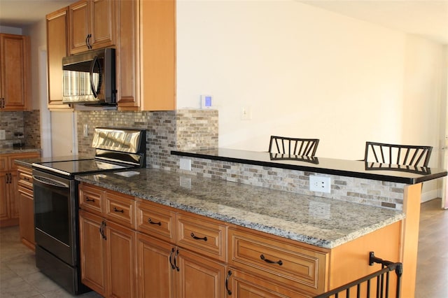 kitchen with a kitchen bar, stainless steel electric range, light stone counters, and decorative backsplash