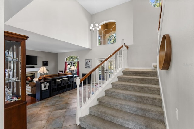 stairway with a towering ceiling, a chandelier, and a healthy amount of sunlight