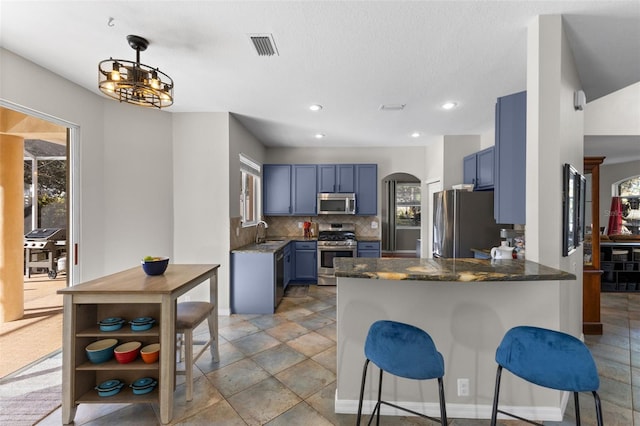 kitchen featuring stainless steel appliances, blue cabinetry, kitchen peninsula, sink, and backsplash