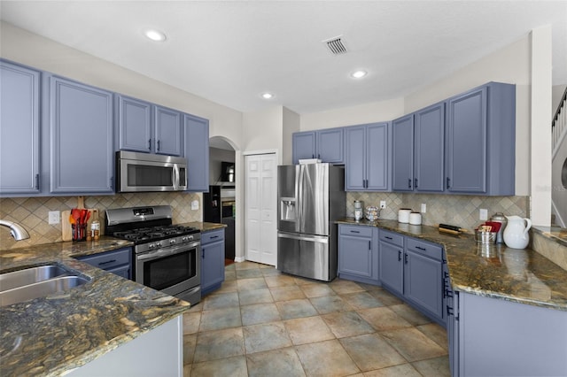 kitchen with kitchen peninsula, tasteful backsplash, blue cabinetry, appliances with stainless steel finishes, and sink