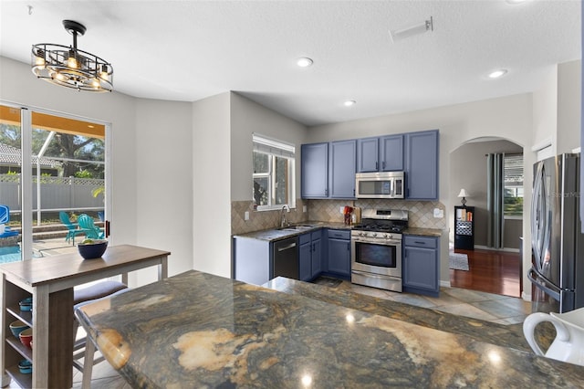 kitchen with stainless steel appliances, blue cabinetry, sink, decorative light fixtures, and tasteful backsplash