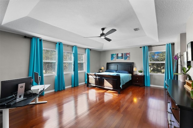 bedroom with ceiling fan, a raised ceiling, a textured ceiling, and hardwood / wood-style flooring