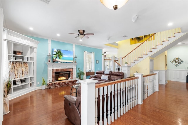 living area featuring ceiling fan, stairway, ornamental molding, a fireplace, and wood finished floors