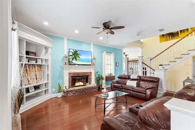 living room featuring visible vents, ornamental molding, a brick fireplace, and wood finished floors