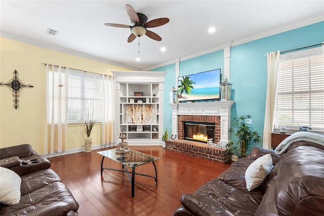 living room featuring visible vents, a brick fireplace, ornamental molding, and hardwood / wood-style flooring