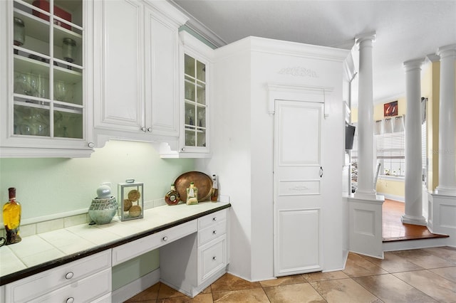 kitchen with glass insert cabinets, white cabinetry, light tile patterned floors, decorative columns, and tile counters