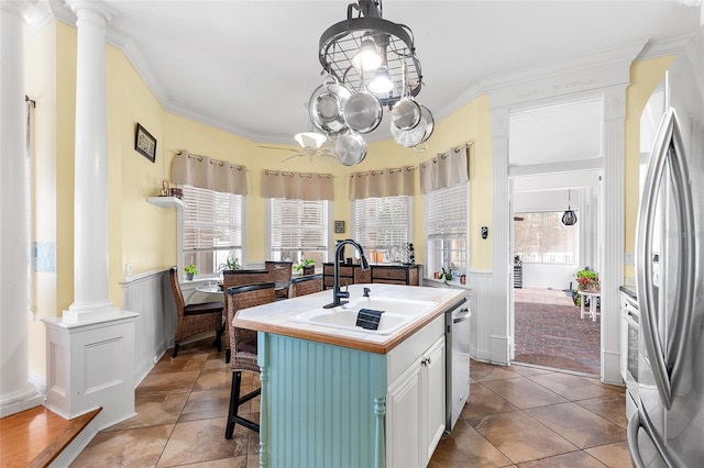 kitchen featuring decorative columns, a sink, stainless steel appliances, wainscoting, and crown molding