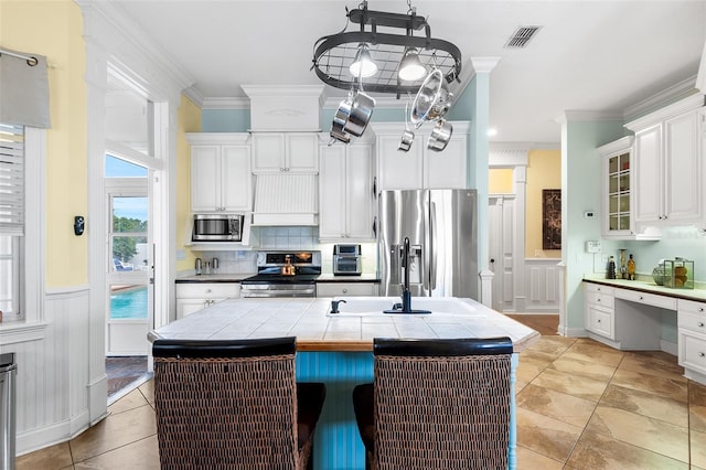 kitchen featuring a sink, stainless steel appliances, tile counters, built in desk, and crown molding