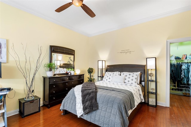 bedroom featuring hardwood / wood-style floors, a ceiling fan, baseboards, a walk in closet, and crown molding