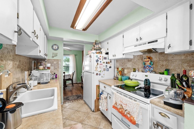 kitchen with sink, white appliances, light tile patterned floors, white cabinetry, and decorative backsplash