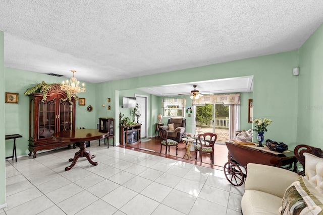 living room with ceiling fan with notable chandelier, light tile patterned floors, and a textured ceiling