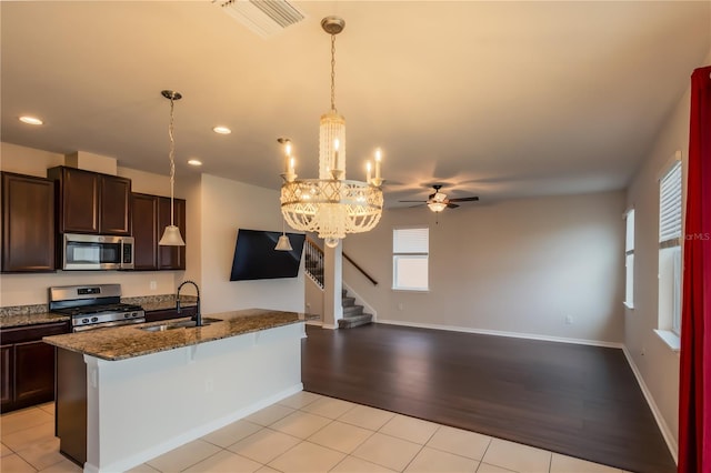 kitchen with ceiling fan with notable chandelier, appliances with stainless steel finishes, dark stone countertops, sink, and light tile patterned floors