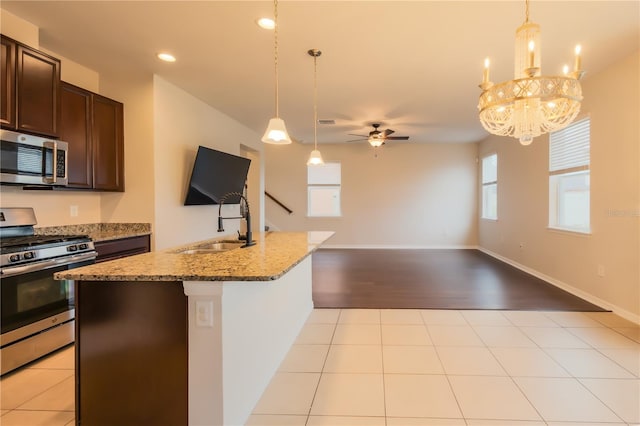 kitchen with ceiling fan with notable chandelier, dark brown cabinetry, stainless steel appliances, sink, and light stone counters