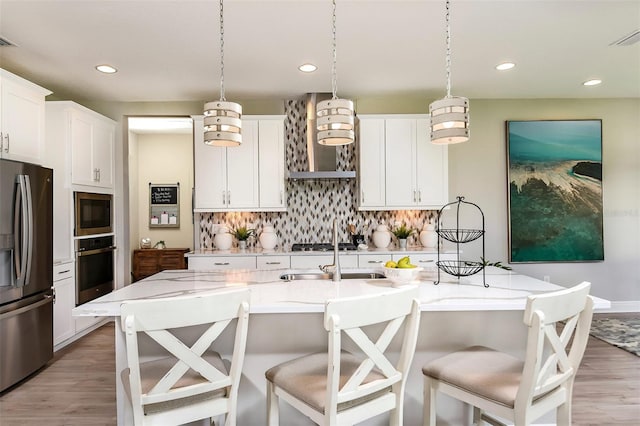 kitchen featuring white cabinetry, stainless steel appliances, an island with sink, decorative light fixtures, and decorative backsplash