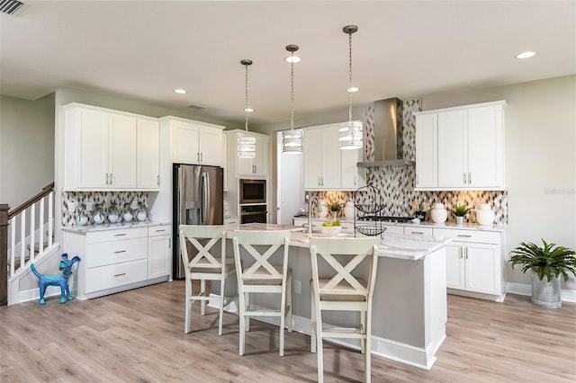 kitchen featuring white cabinets, an island with sink, stainless steel appliances, and wall chimney range hood