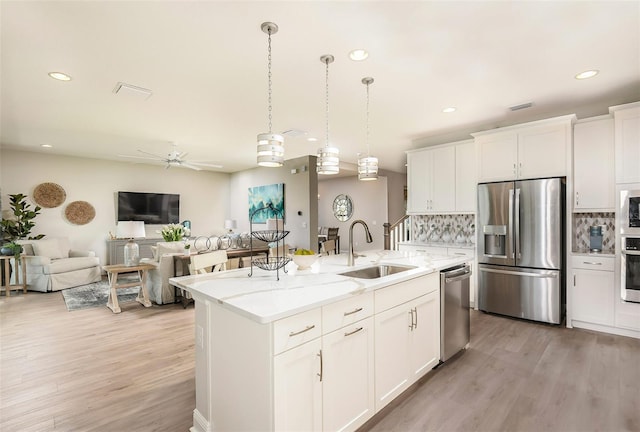 kitchen featuring stainless steel appliances, an island with sink, decorative light fixtures, decorative backsplash, and white cabinets