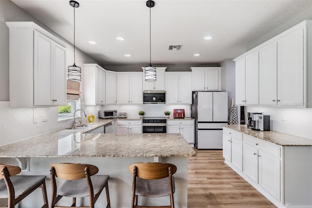 kitchen with stainless steel appliances, sink, white cabinets, light hardwood / wood-style floors, and hanging light fixtures