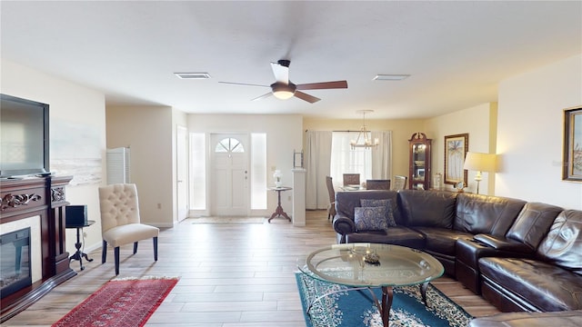 living room featuring ceiling fan with notable chandelier and light hardwood / wood-style flooring