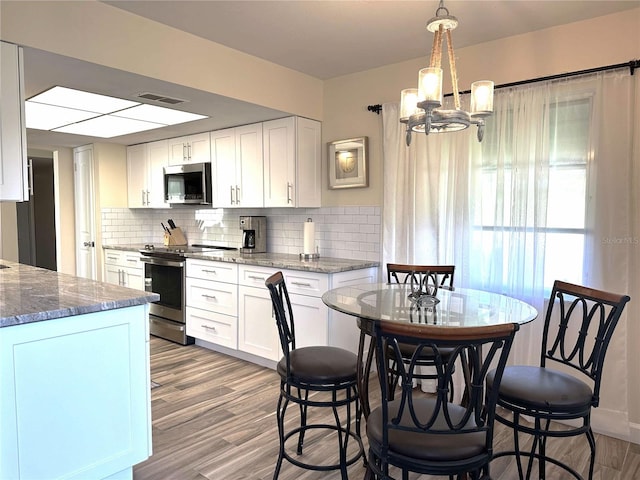 kitchen with tasteful backsplash, white cabinetry, stainless steel appliances, and decorative light fixtures