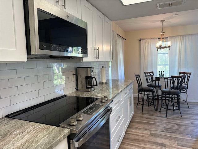 kitchen featuring white cabinets, decorative backsplash, stainless steel appliances, and an inviting chandelier