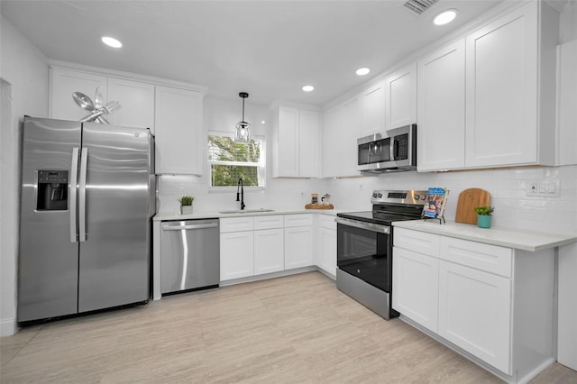 kitchen with appliances with stainless steel finishes, sink, white cabinets, decorative light fixtures, and tasteful backsplash