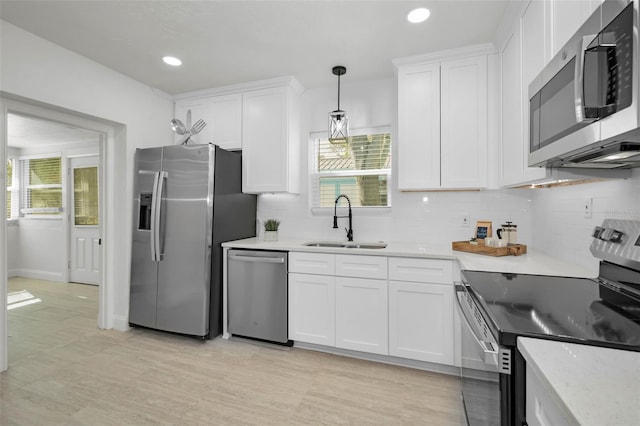 kitchen featuring sink, stainless steel appliances, white cabinetry, and hanging light fixtures