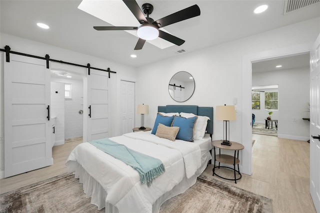 bedroom with a closet, ceiling fan, a barn door, and light hardwood / wood-style flooring