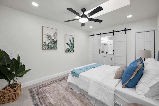 bedroom featuring ceiling fan, a barn door, and light hardwood / wood-style flooring