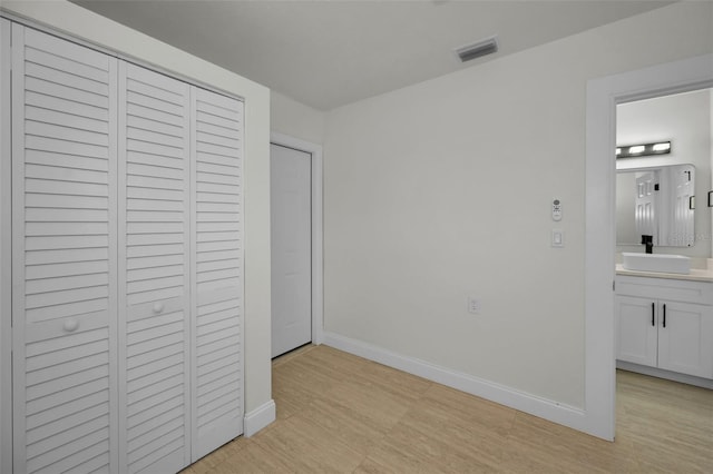 unfurnished bedroom with ensuite bath, a closet, light hardwood / wood-style floors, and sink