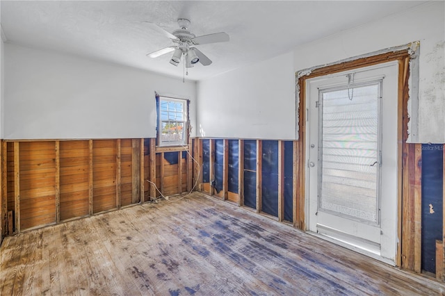 empty room with wood-type flooring, wooden walls, and ceiling fan