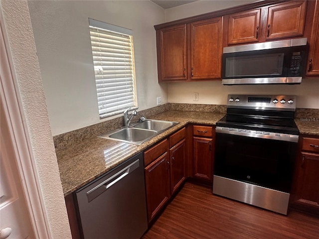 kitchen with stainless steel appliances, a sink, dark wood-style floors, brown cabinetry, and dark countertops