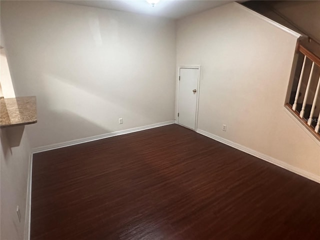 empty room featuring dark wood-style flooring, stairway, and baseboards