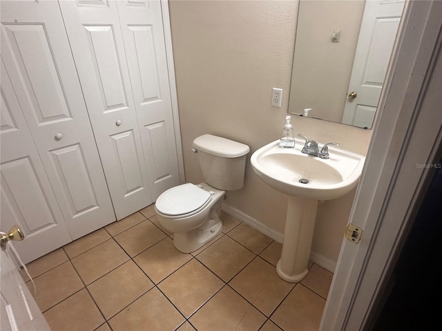 half bath with baseboards, a sink, toilet, and tile patterned floors