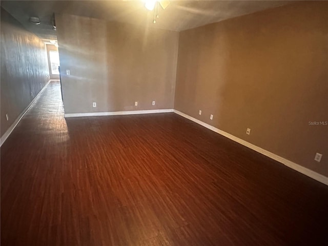 unfurnished room featuring a ceiling fan, baseboards, and dark wood-style flooring