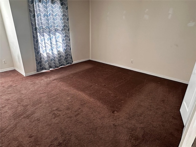 unfurnished room featuring dark colored carpet and baseboards