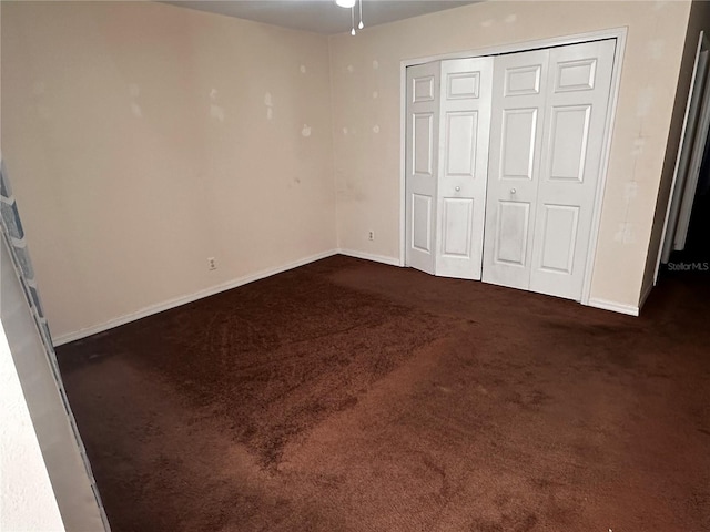 unfurnished bedroom with dark colored carpet, a closet, and baseboards