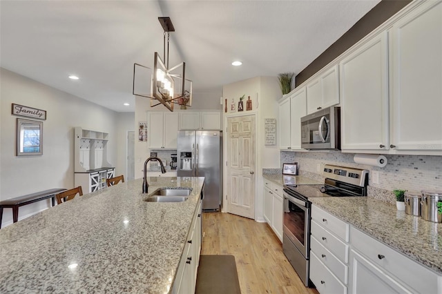 kitchen featuring white cabinetry, stainless steel appliances, decorative light fixtures, light stone counters, and sink