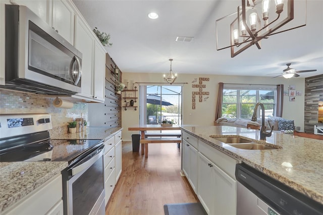 kitchen featuring appliances with stainless steel finishes, hanging light fixtures, light stone countertops, white cabinets, and sink