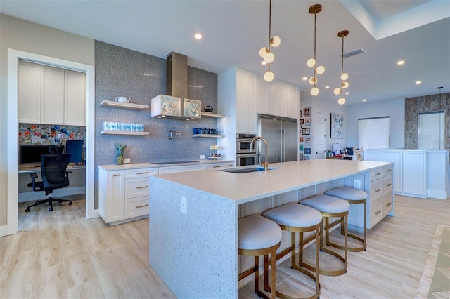 kitchen with built in desk, tasteful backsplash, white cabinets, stainless steel appliances, and a center island with sink