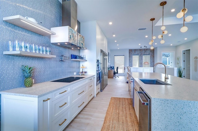 kitchen with wall chimney exhaust hood, sink, white cabinetry, hanging light fixtures, and stainless steel appliances