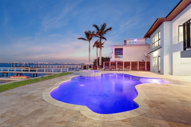 pool at dusk featuring a patio area, pool water feature, and a water view