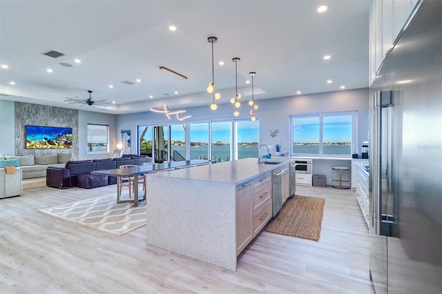 kitchen featuring a spacious island, a water view, hanging light fixtures, ceiling fan, and light stone countertops