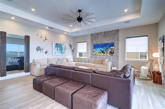 living room featuring a tray ceiling, light hardwood / wood-style flooring, a healthy amount of sunlight, and a water view